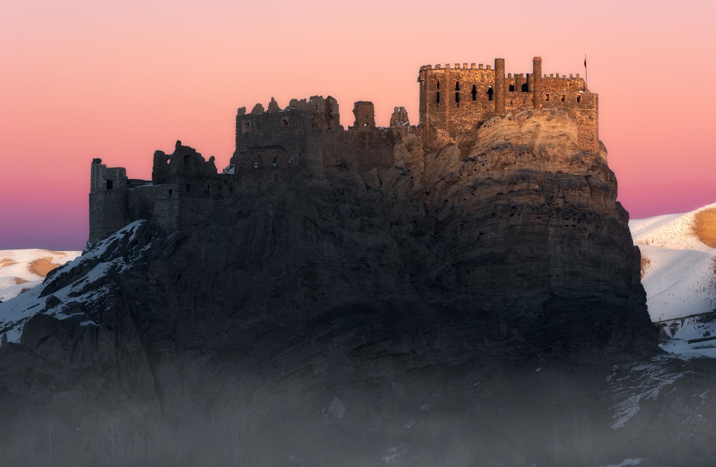 A ruined stone castle surrounded by snow at dusk