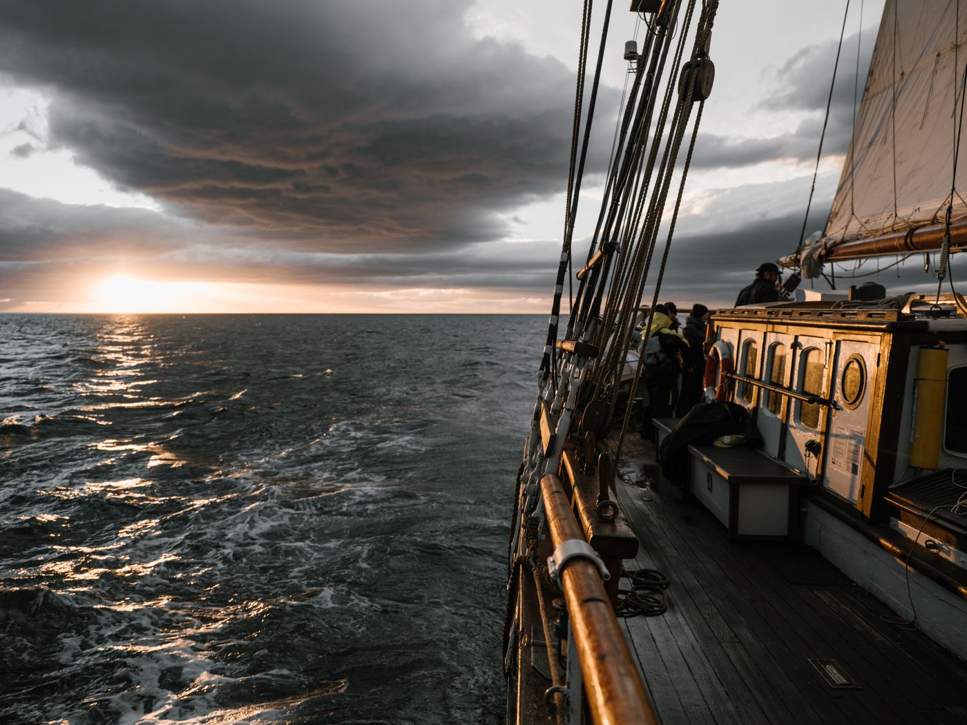 A view over the bow of a wooden ship at sunset, illustrating escape by sea.